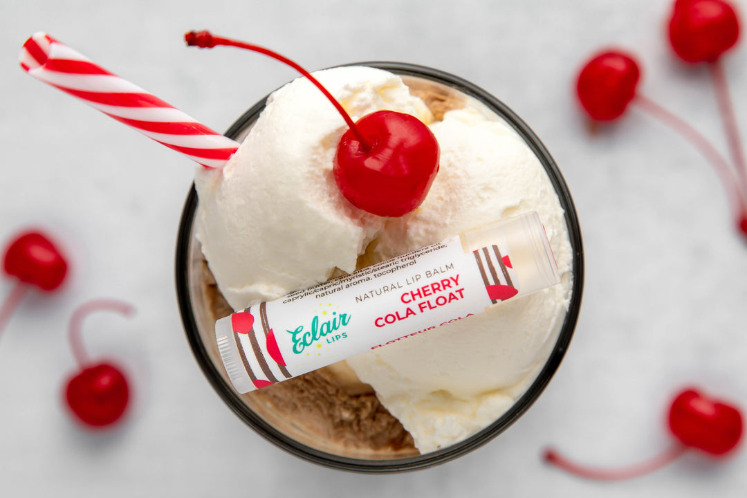 A tube of Eclair Lips Cherry Cola Float lip balm atop a cherry cola float