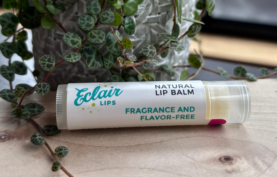 a tube of Eclair Lips fragrance free lip balm resting on a wooden surface in front of a small potted plant
