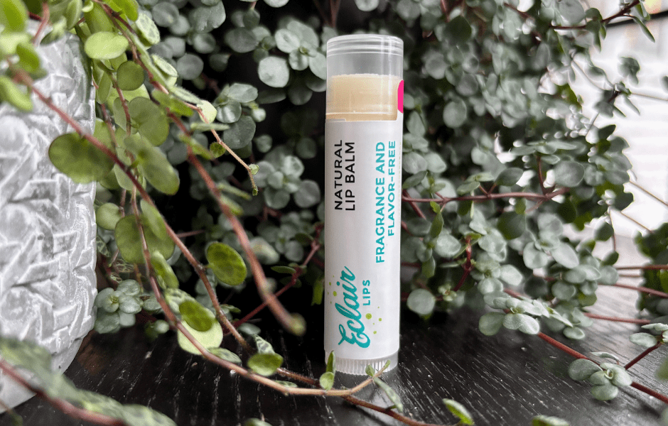 An Eclair Lips Fragrance Free Lip Balm stands on a black wooden surface with tendrils of plants in the background
