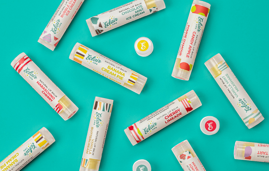 A flat lay of various Eclair Lips natural lip balms in different sweet and fruity flavors, scattered across a vibrant teal background.
